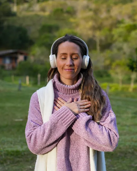 Mari de olhos fechados, com fones e as mãos sobre o peito